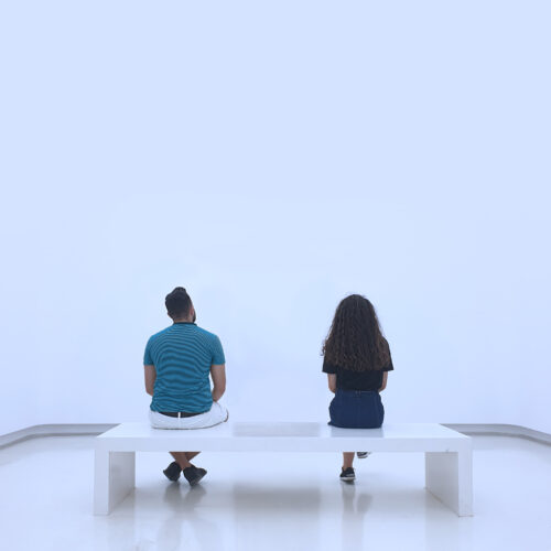 Two people sitting on bench looking toward a blank wall